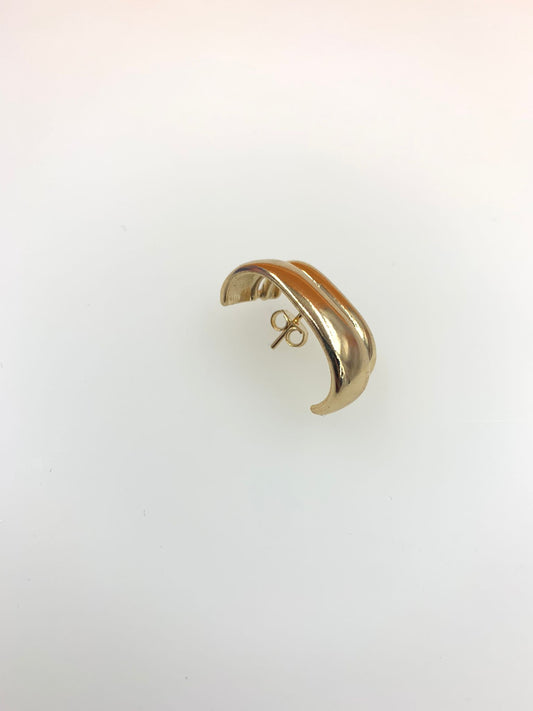 A sleek gold dome huggie earring rests against a neutral white background.