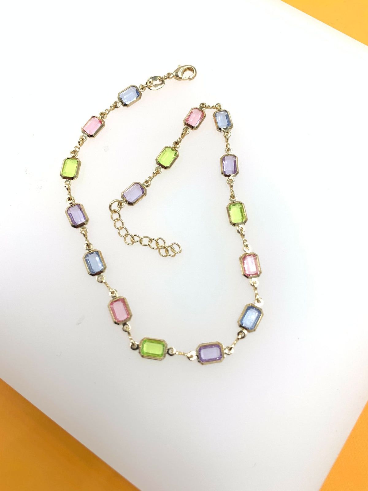 A delicate gold-plated chain bracelet features colorful emerald-cut gemstones in shades of pink, blue, green, and purple.