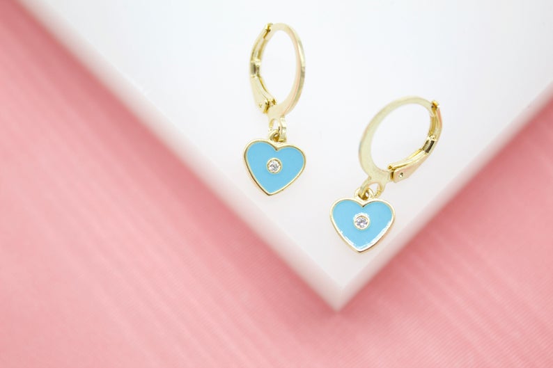 A pair of gold huggie hoop earrings features dangling light blue enamel heart charms accented with small sparkling diamonds.