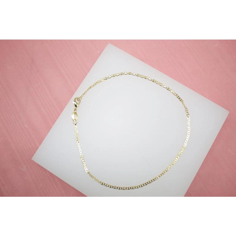 A delicate gold chain bracelet rests on a white display card against a pink background.