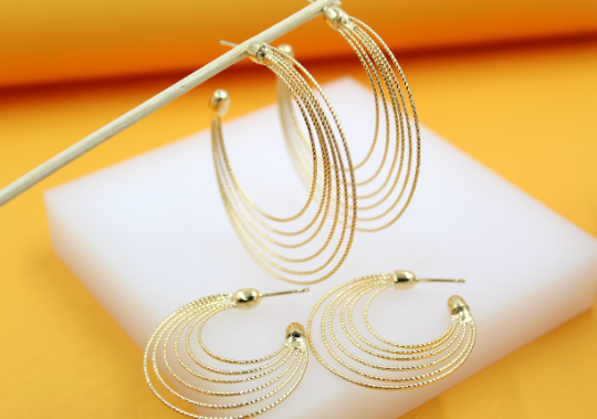 A pair of elegant multi-strand gold hoop earrings rests on a white display block.