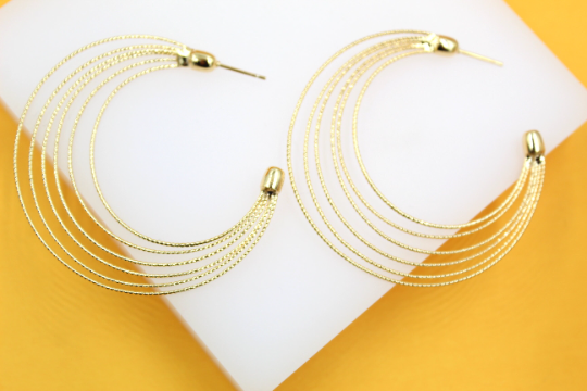 A pair of elegant multi-strand gold hoop earrings rests on a white display against a vibrant yellow background.