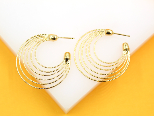 A pair of multi-strand gold hoop earrings rests against a white and yellow background.