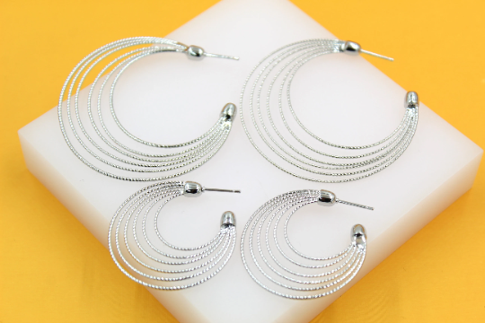 Four multi-strand silver hoop earrings rest on a white display block against a vibrant yellow background.