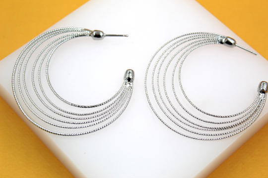 A pair of multi-strand silver hoop earrings rests on a white display against a yellow background.