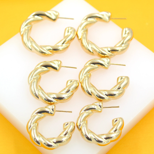 Three pairs of shiny gold twisted hoop earrings rest on a white display against a vibrant yellow background.