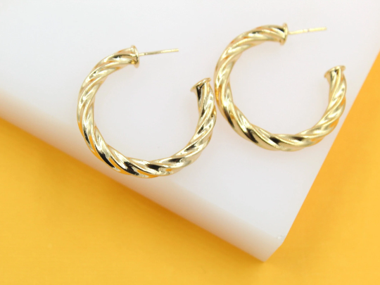 A pair of polished gold twist hoop earrings rests elegantly on a white surface against a bright yellow background.