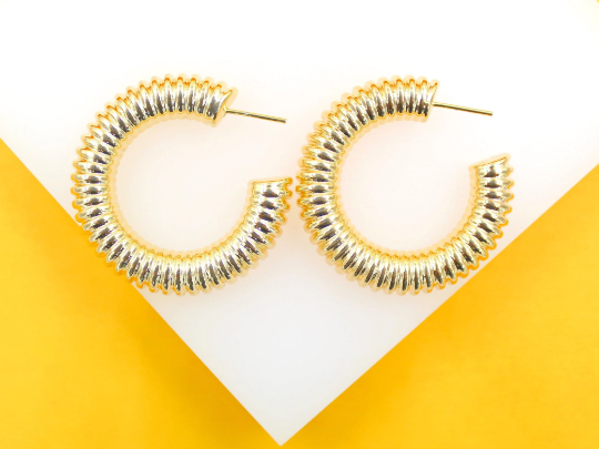 A pair of ribbed gold hoop earrings rests on a white display against a vibrant yellow background.