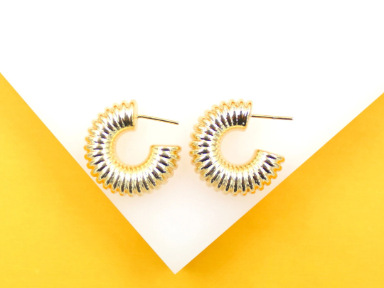 A pair of shiny gold ribbed hoop earrings rests against a white and yellow background.