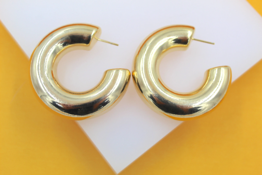 A pair of thick, polished gold hoop earrings rests on a white and yellow surface.