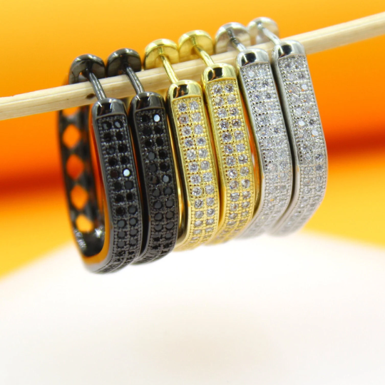 Three pairs of dazzling pave hoop earrings in black, gold, and silver hang neatly from a wooden display stick.
