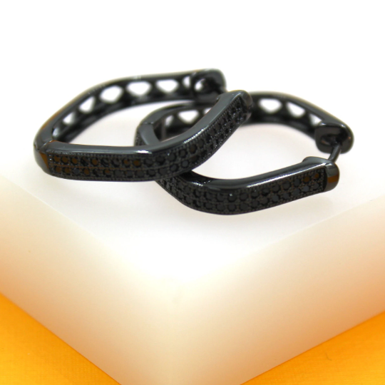 A pair of black geometric pave hoop earrings rests on a white display surface.