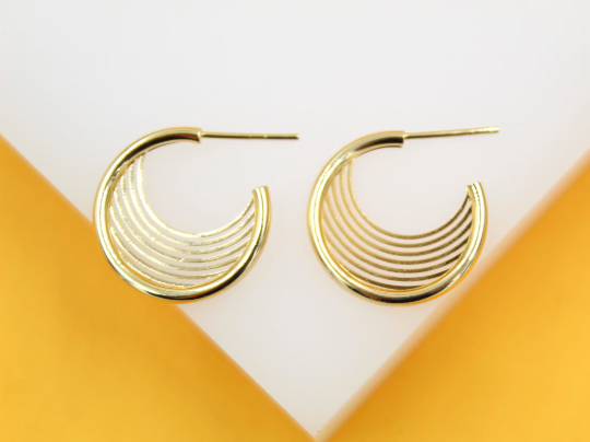 A pair of polished gold multi-strand hoop earrings rests on a white and yellow display block.