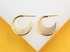 A pair of polished gold multi-strand hoop earrings rests on a white and yellow display block.