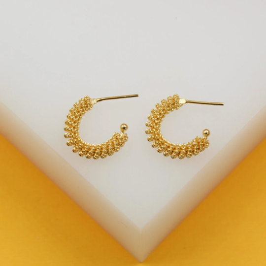 A pair of textured gold hoop earrings rests neatly on a white and yellow display stand.
