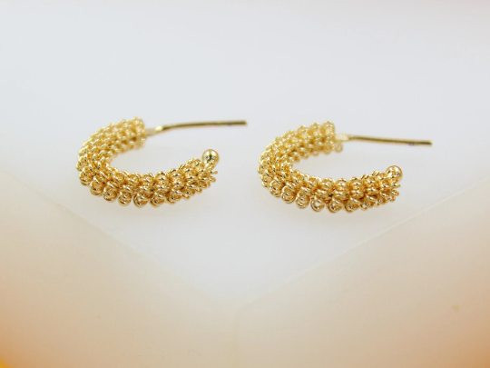 A pair of gold textured hoop earrings rest on a white surface.