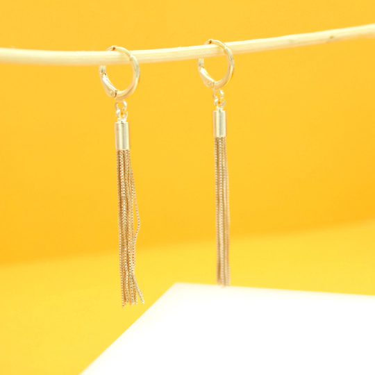 A pair of elegant gold tassel earrings hangs delicately from a thin stick against a vibrant yellow background.