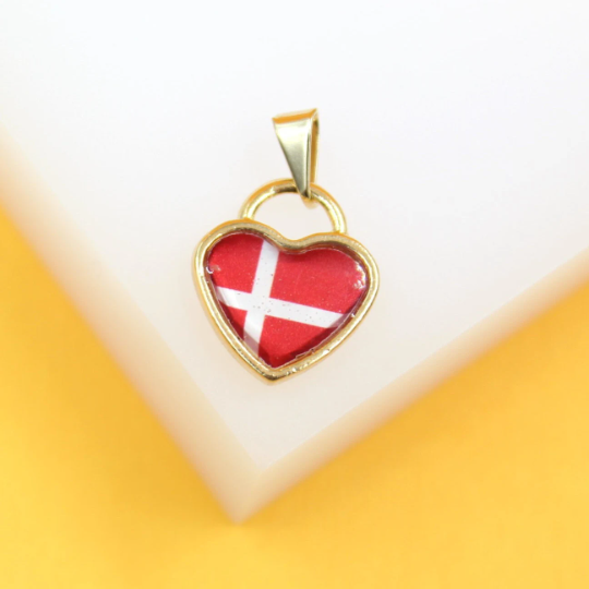 A gold heart-shaped pendant featuring the Danish flag rests on a white and yellow surface.