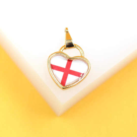 A gold heart-shaped pendant featuring the red cross flag of England rests on a white and yellow surface.