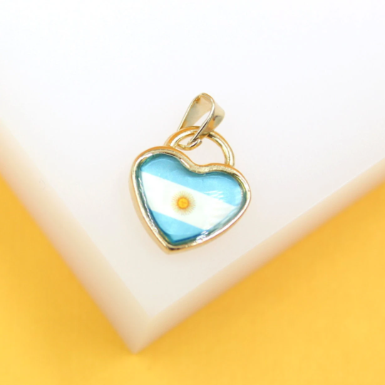 A gold-rimmed heart-shaped pendant featuring the flag of Argentina rests on a white and yellow surface.