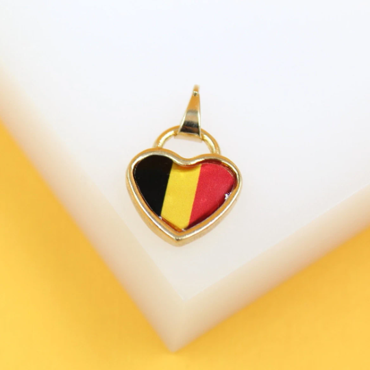 A gold heart-shaped pendant featuring the flag of Belgium rests on a white surface against a yellow background.