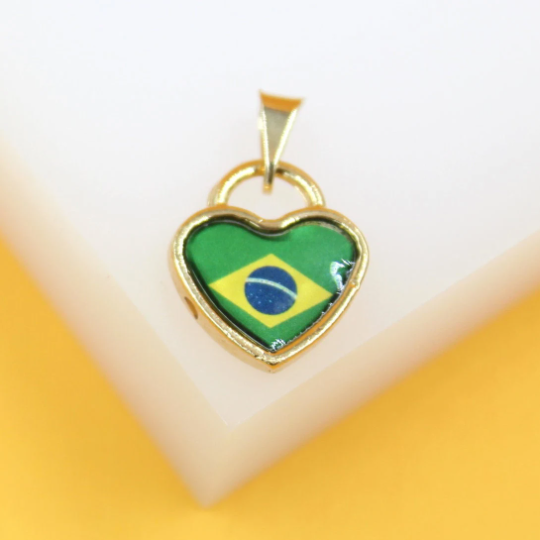 A gold heart-shaped pendant featuring the Brazilian flag rests on a white display surface.