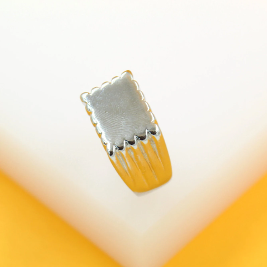 A unique gold ring features a scalloped rectangular silver setting engraved with a fingerprint design.