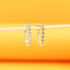 A pair of gold hoop earrings embellished with sparkling cubic zirconia stones rests horizontally on a wooden stick against a bright yellow background.