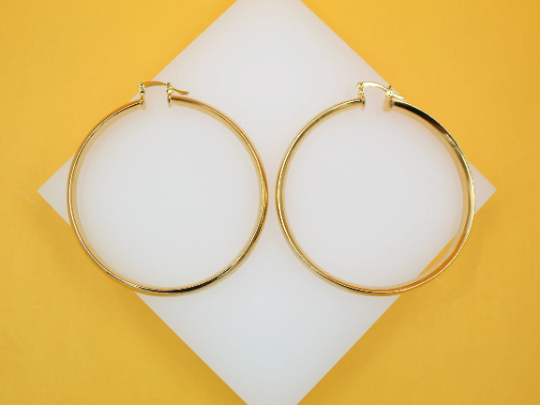 A pair of classic gold hoop earrings rests neatly on a white display surface against a vibrant yellow background.