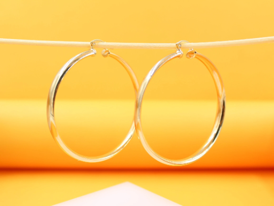 Two large, polished gold hoop earrings hang delicately from a thin string against a vibrant yellow background.