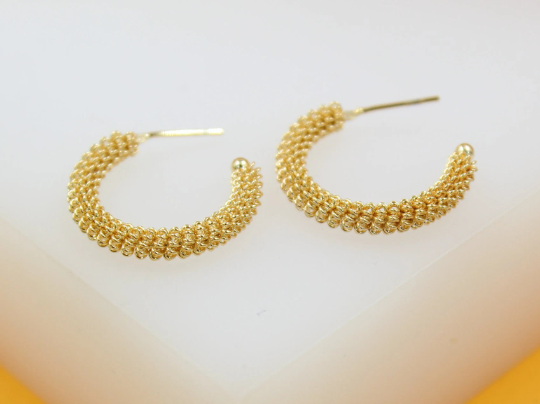 A pair of textured gold hoop earrings rests neatly on a clean white display surface.