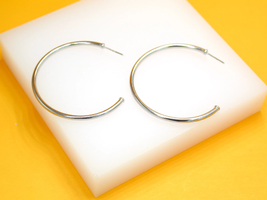 A pair of sleek silver hoop earrings rests on a white display block against a vibrant yellow background.