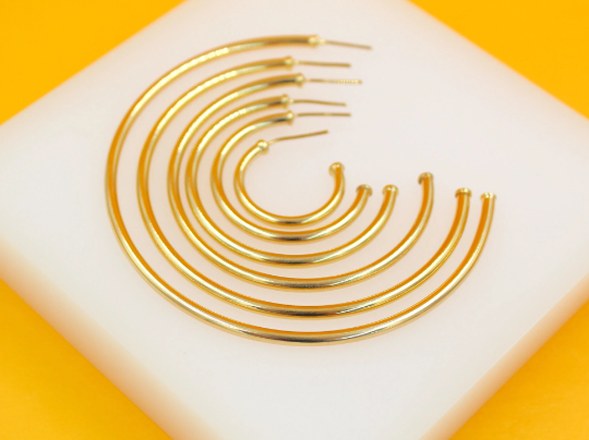 A graduated set of polished gold-plated hoop earrings rests on a white display stand against a vibrant yellow background.