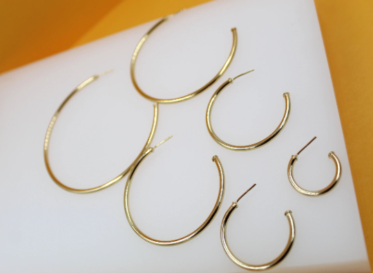A set of five graduating gold hoop earrings rests neatly on a white display block against an orange backdrop.