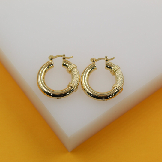 A pair of gold hoop earrings with textured accents rests on a white display surface.