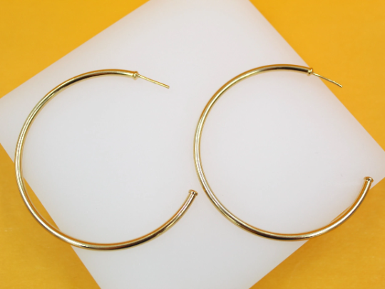 A pair of sleek gold hoop earrings rests neatly on a white display against a vibrant yellow background.