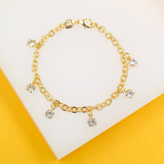 A delicate gold chain bracelet features sparkling crystal charms dangling against a white and yellow background.