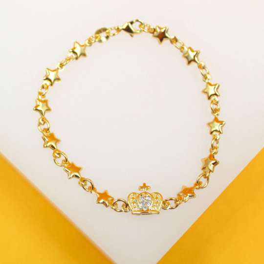 A gold charm bracelet featuring alternating star links and a central crown charm encrusted with cubic zirconia stones is displayed on a light surface.
