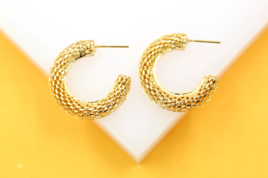 A pair of textured gold half-hoop earrings rests on a white and yellow surface.