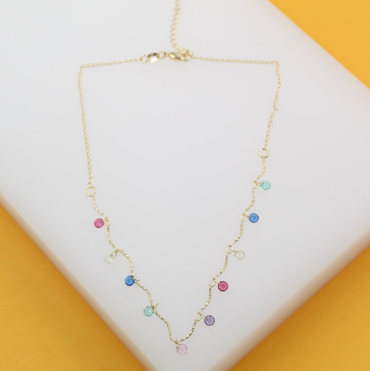 A delicate gold chain necklace features scattered colorful gemstone charms resting on a white display surface.