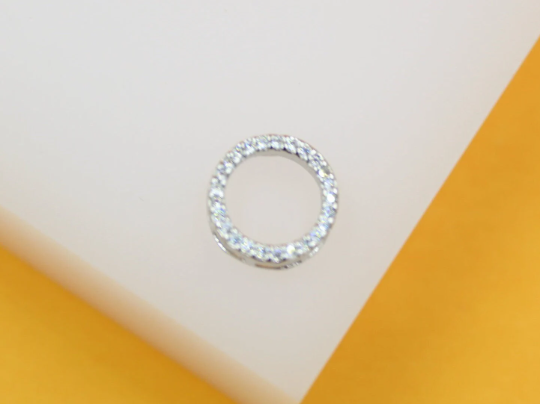 A round, silver pendant encrusted with sparkling cubic zirconia rests against a white and yellow background.