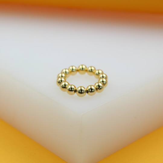 A shiny gold bead ring rests on a white and yellow display surface.