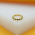A shiny gold bead ring rests on a white and yellow display surface.
