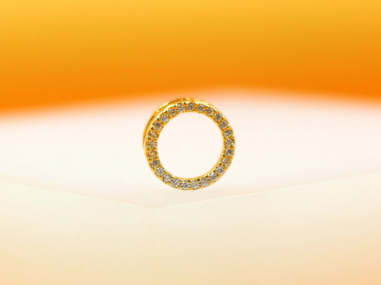 A gold circle pendant encrusted with sparkling cubic zirconia stones rests against a soft gradient background.