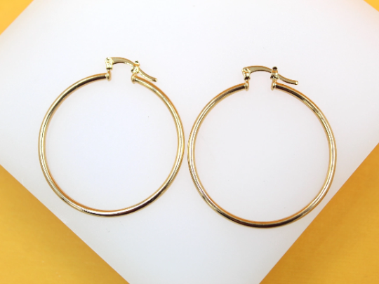 A pair of polished gold hoop earrings rests on a white display surface.