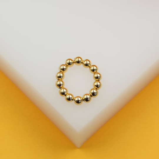 A polished gold beaded ring rests gracefully on a white display against a vibrant yellow background.