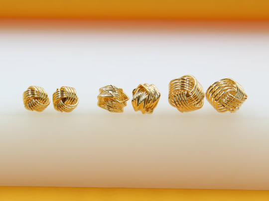 Three pairs of shiny gold wire-wrapped knot stud earrings display in graduating sizes on a white and orange display surface.