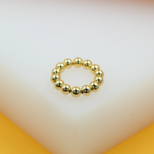 A shiny gold beaded ring rests on a white and yellow display surface.