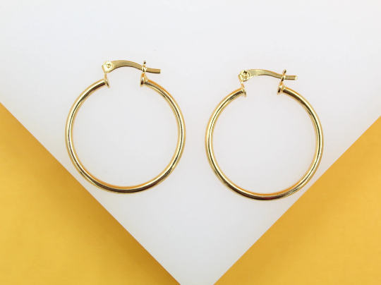 A pair of polished gold hoop earrings rests against a white and yellow background.