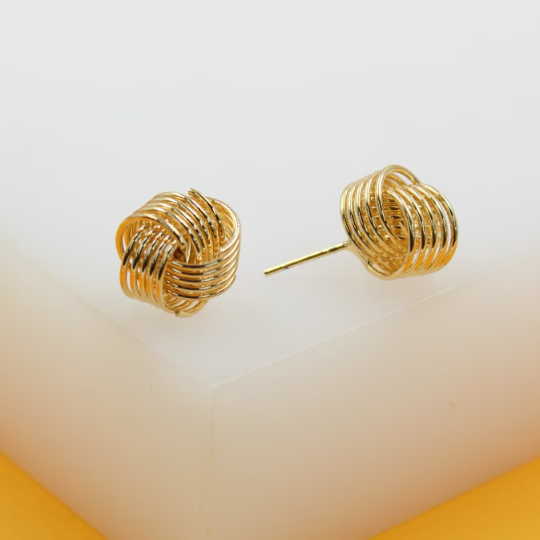 A pair of polished gold-plated love knot stud earrings rests on a clean white display block.